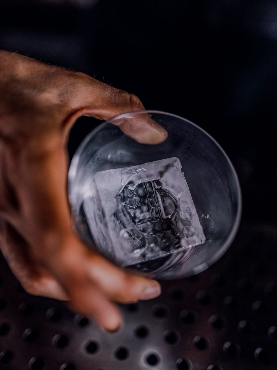 Un glaçon transparent taillé, tenu dans un verre